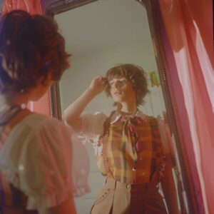 Person trying on a femboy outfit in front of a mirror, reflecting the beginning of their fashion exploration.
