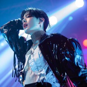 K-pop idol in an androgynous outfit, posing on stage. Represents the influence of K-pop and J-fashion on femboy fashion.